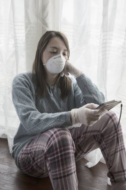Kilitleme modundaki genç imajını algıla. Karantina emirleri sırasında evde kalmanın sıkıntısını gösteren maskeli, eldivenli ve cep telefonlu bir genç kızın konsept fotoğrafı..