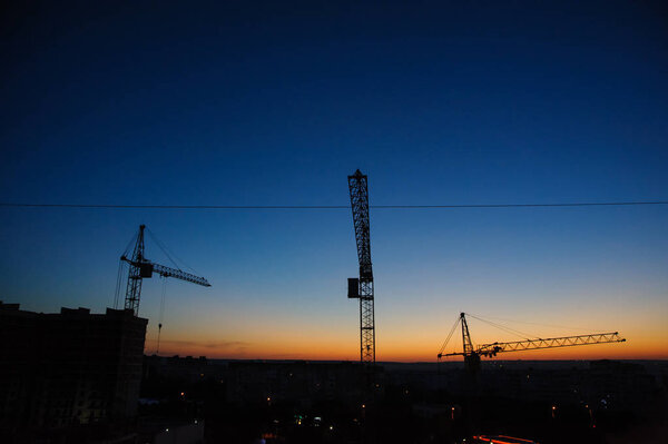 Силуэт башенных кранов на строительной площадке
