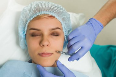 Top view of lips augmentation procedure on a young woman done by a cosmetologist doctor with Hyaluronic acid Injection.