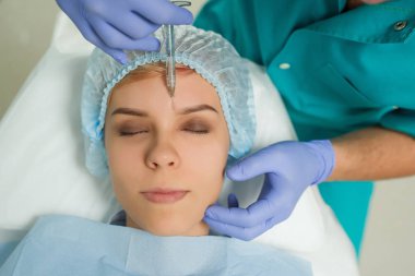 Kozmetolog bir doktorun Hyaluronic asit enjeksiyonuyla gerçekleştirdiği genç bir kadın üzerinde ilave prosedürün yan görüşü.