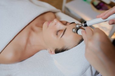 Kadının yüz masajı spa prosedürünün yan görüntüsü. Elektrikli yüz bakımı. Mikroakım kaldırma suratı. Güzellik spa prosedürü. Sağlık odasında yaşlanma karşıtı gençleştirme cerrahi olmayan tedavi