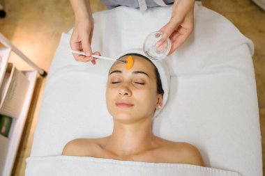 Kadının tedavi edici yüz masajı yaptırırken yakın plan fotoğrafı. Yüzünde fırçayla maske takan bir terapist..