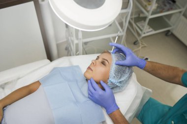 Kozmetolog bir doktorun Hyaluronic asit enjeksiyonuyla gerçekleştirdiği genç bir kadın üzerinde ilave prosedürün yan görüşü.