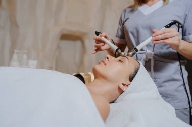 Kadının yüz masajı spa prosedürünün yan görüntüsü. Elektrikli yüz bakımı. Mikroakım kaldırma suratı. Güzellik spa prosedürü. Sağlık odasında yaşlanma karşıtı gençleştirme cerrahi olmayan tedavi
