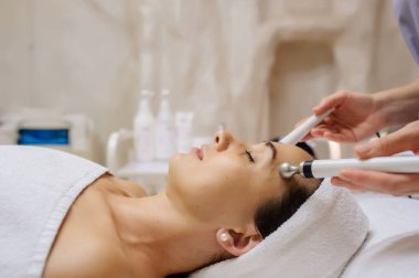 Kadının yüz masajı spa prosedürünün yan görüntüsü. Elektrikli yüz bakımı. Mikroakım kaldırma suratı. Güzellik spa prosedürü. Sağlık odasında yaşlanma karşıtı gençleştirme cerrahi olmayan tedavi