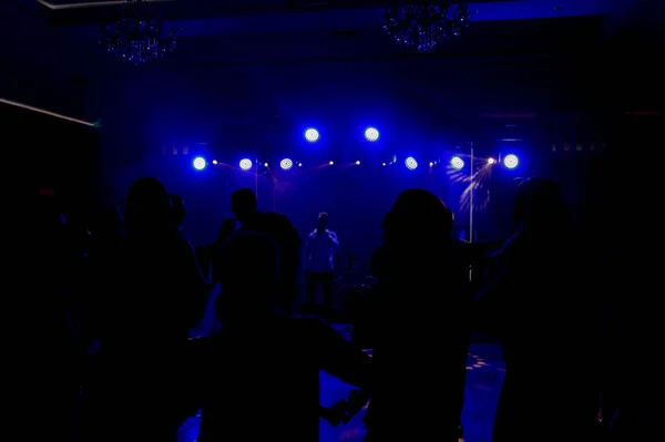 在黑暗中 在一个舞台前 蓝色的光芒照耀着跳舞的人们 舞台上有一个乐队和一个歌手 — 图库照片
