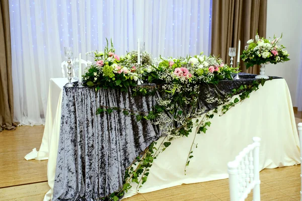 白とグレーのテーブルクロス フラワーアレンジメント付きのウェディングプレシディアムテーブル 白い花瓶の花束O花 シルバーサポートのキャンドル 背景に白い椅子とグレーのカーテン — ストック写真