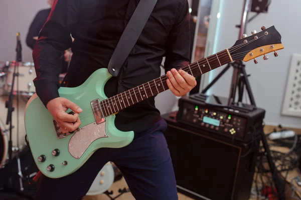 Closeup photo of a player on a green bass giuitar with drums and music desk on background