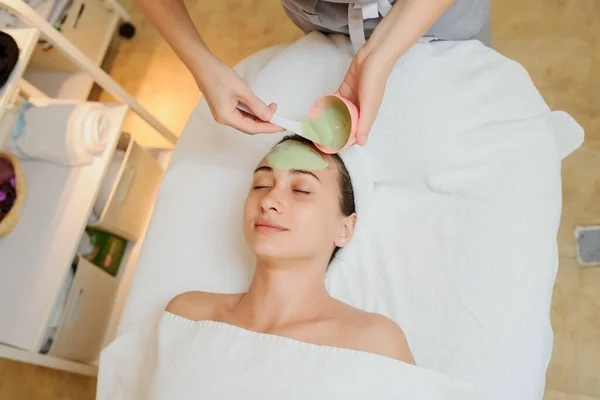 一名戴绿色面具的妇女的近照 将口罩涂在皮肤和额头上的治疗师 — 图库照片