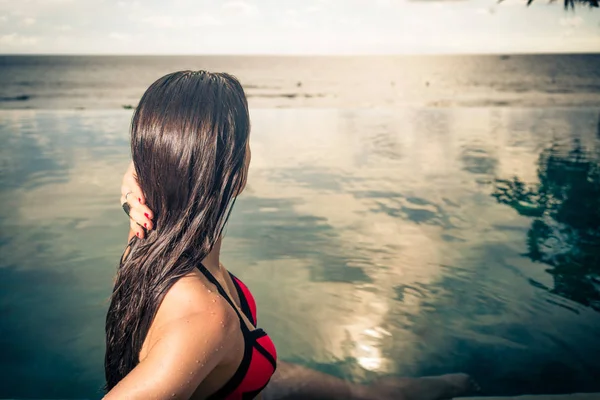 Mujer con bikini rojo y flor en pelo en piscina infinita —  Fotos de Stock