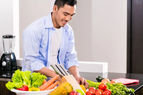 Aziatisch mens snijden groenten en salade — Stockfoto