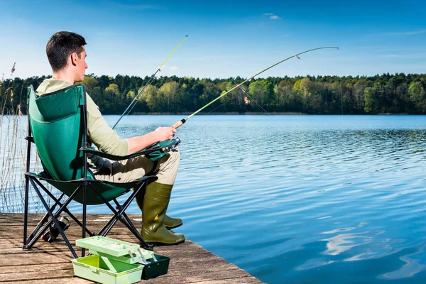 Человек рыбачит на озере сидя на пристани — стоковое фото