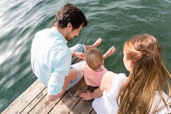 Família sentada na água pendurada pés na lagoa — Fotografia de Stock