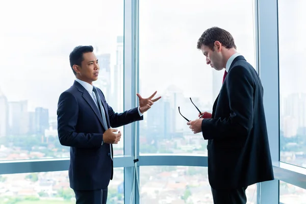 Businessmen standing in front of office window — Stock Photo, Image
