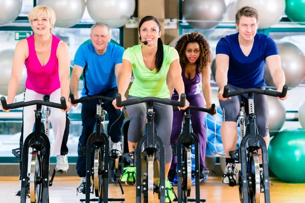 Фитнес-группа мужчин и женщин, крутящихся на велосипеде в тренажерном зале — стоковое фото