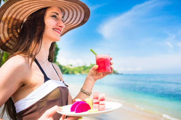 Mujer en la playa tropical comiendo fruta para el desayuno —  Fotos de Stock