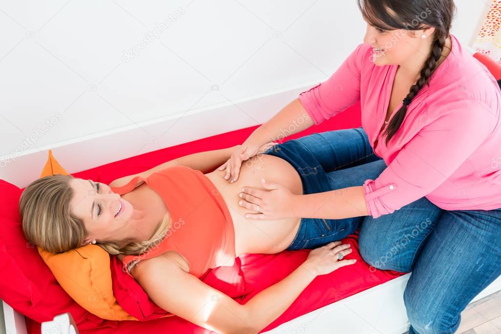 Midwife exanimating belly of pregnant woman manually