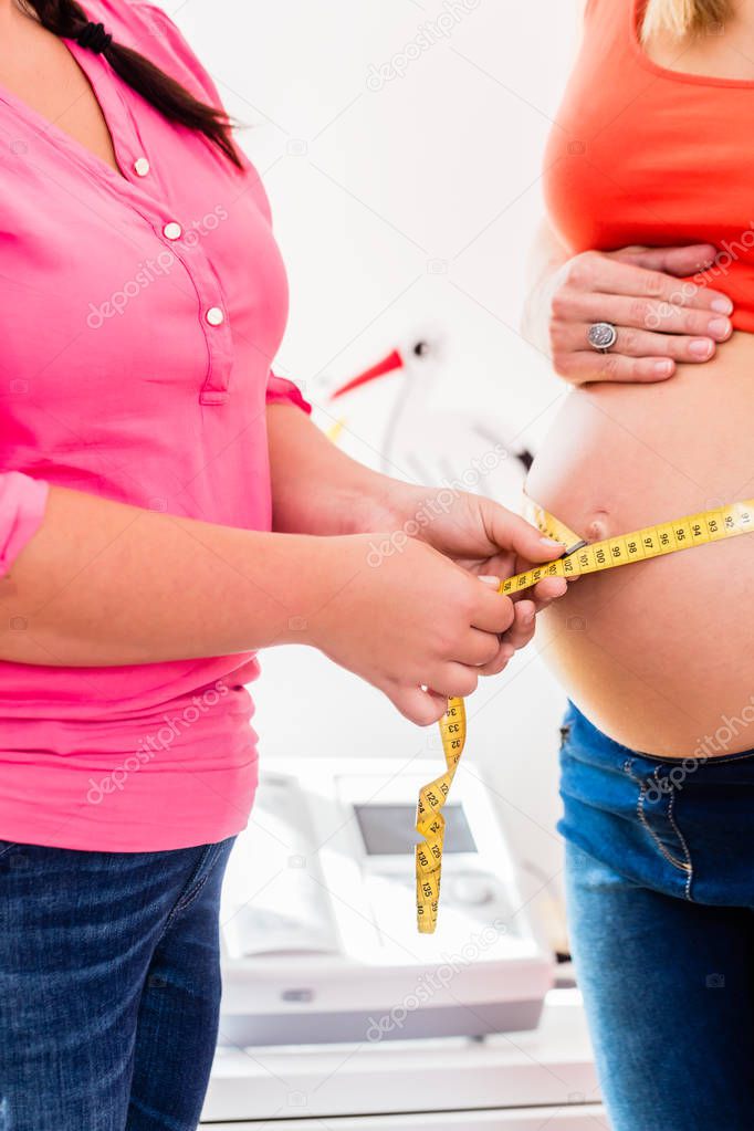 Standing pregnant women and midwife measuring circumference