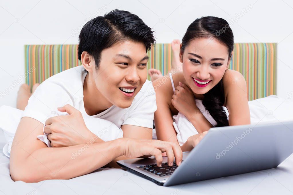 Asian couple in bedroom surfing the internet