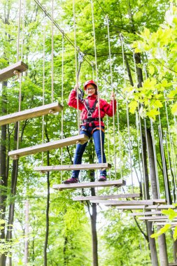 Kid walking on rope bridge in climbing course clipart