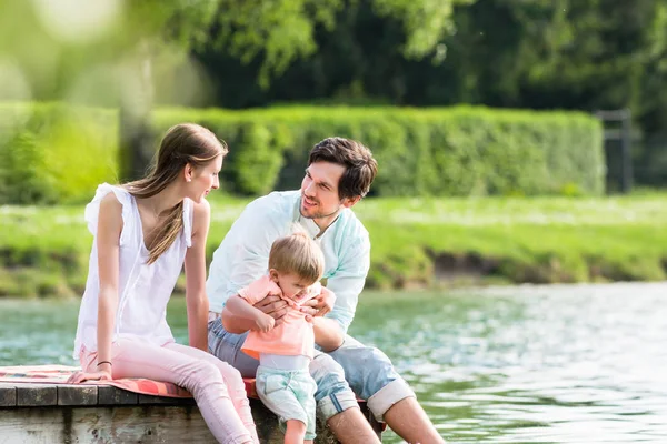 Familia feliz sentada en embarcadero en el lago o estanque — Foto de Stock
