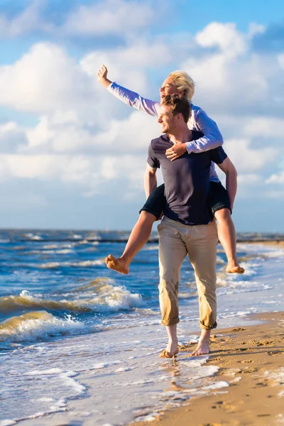 Przeprowadzanie kobieta mężczyzna piggyback na plaży — Zdjęcie stockowe