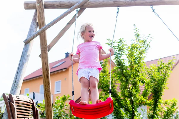 Liten flicka på gunga framför huset — Stockfoto