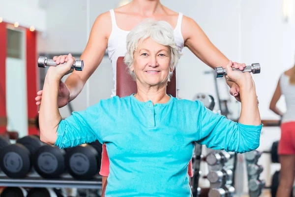 Donna anziana con allenatore in palestra sollevamento manubri — Foto Stock