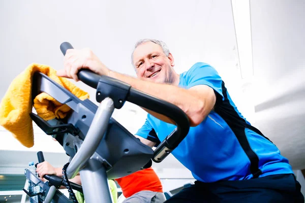 Senior sport op de spinning fiets in de sportschool doet — Stockfoto