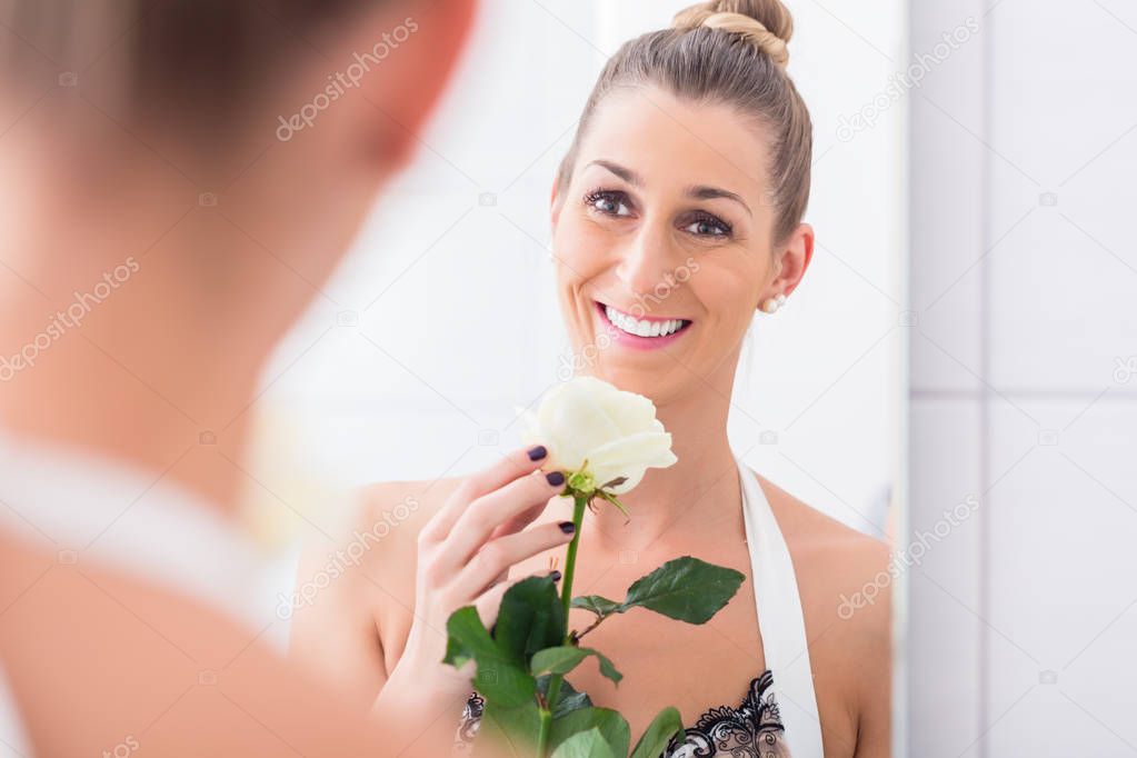 Woman holding white rose regarding herself in the mirror