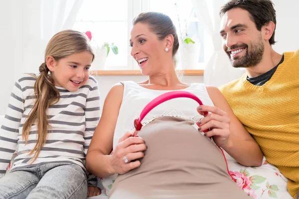 Familie en zwangere mama met behulp van de hoofdtelefoon op de buik van de baby — Stockfoto