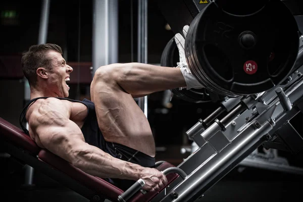 Hombre en el gimnasio de entrenamiento en la pierna prensa — Foto de Stock