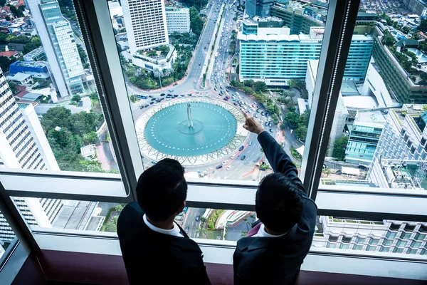 Two Asian businesspeople looking down to city streets — Stock Photo, Image