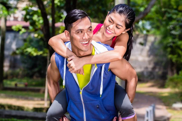 Asiático hombre llevar su novia piggyback para el deporte —  Fotos de Stock