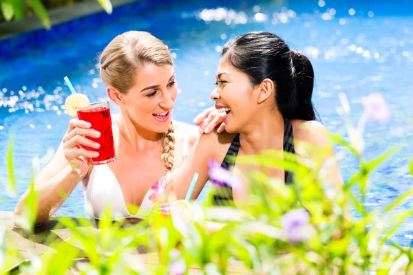 Mulheres na piscina do hotel asiático beber coquetéis — Fotografia de Stock