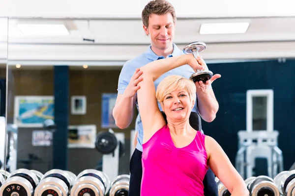 Senior vrouw in sport uitoefenen in de fitnessruimte met trainer — Stockfoto