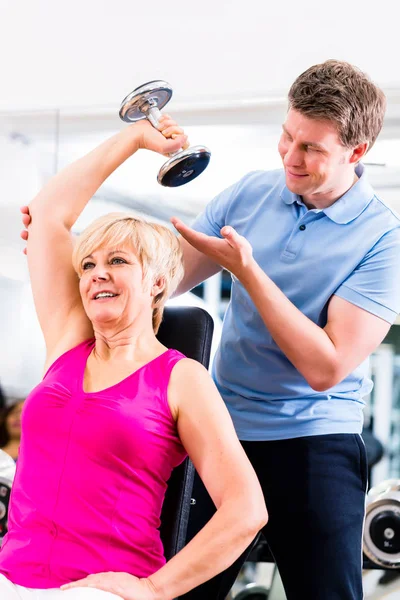 Senior woman at sport exercise in gym with trainer — Stock Photo, Image