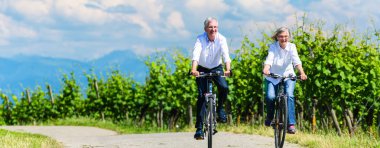 Seniors riding bicycle in vineyard together clipart