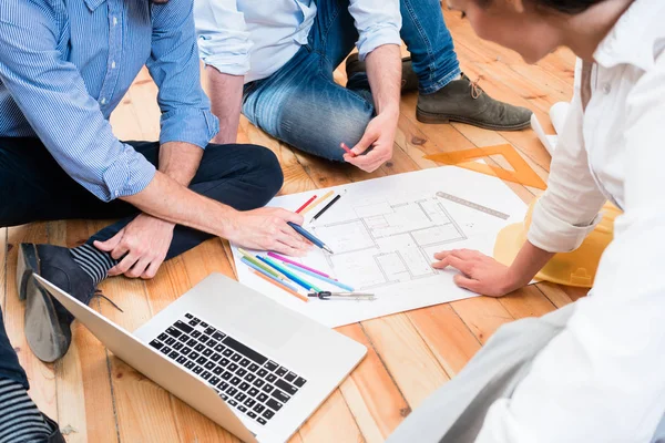 Team of architects sitting on floor with construction plans — Stock Photo, Image