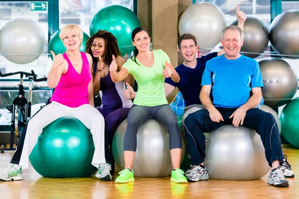 Hombres y mujeres sentados en pelotas de fitness en el gimnasio — Foto de Stock