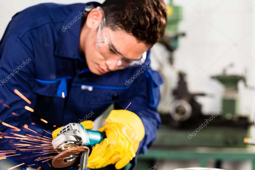 Asian worker grinding metal in manufacturing plant