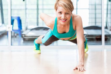 Smiling young woman doing one arm pushup in gym clipart