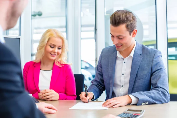 Man signing sales contract for auto at car dealership — Stock Photo, Image