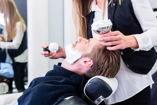 Žena holič holení zákazník ve svém obchodě — Stock fotografie