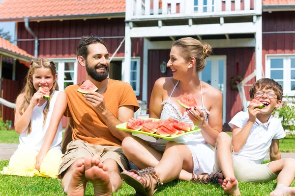 Familie sitzt im Gras im Haus und isst Wassermelone — Stockfoto