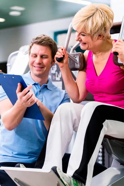 Trainer in de sportschool meewerkende senior vrouw uitoefening — Stockfoto