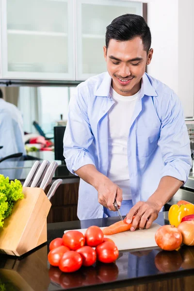 Asian man cutting salad in kitchen — Stock Photo, Image