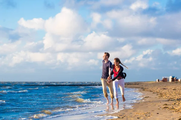 Coppia che corre tra sabbia e onde in spiaggia — Foto Stock