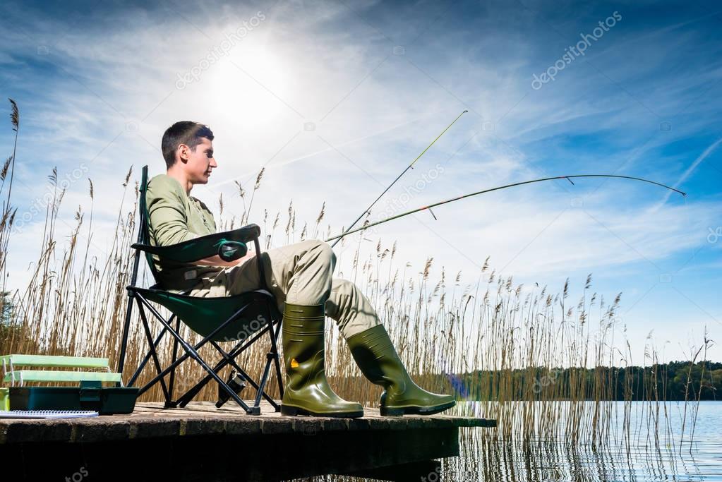 Man fishing at lake sitting on jetty