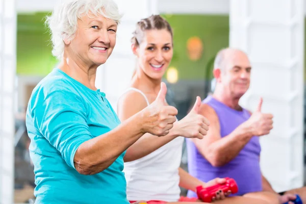 Seniorzy z trenerem w siłowni hotelu sport podnoszenia brzana — Zdjęcie stockowe